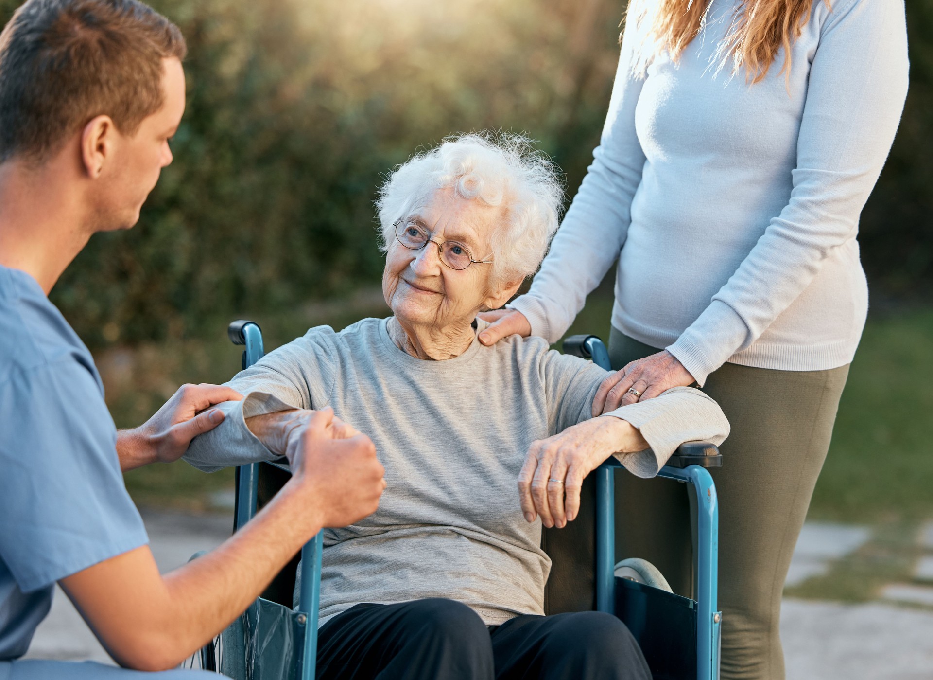Support, caregiver and senior woman in wheelchair with help, medical healthcare and disability assistance from male nurse. Volunteer worker, adult daughter and disabled patient on nursing home estate